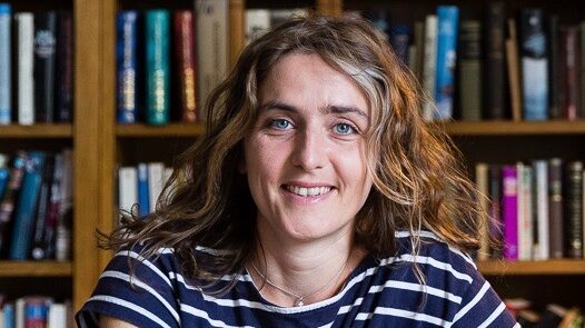 Smiling woman with a striped T-shirt in front of a wall of books