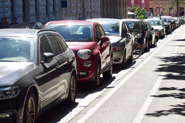 Parked cars on a sidewalk, historic houses in the background.