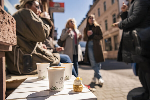 Drei Tassen Kaffee to Go und ein Mini-Cupcake stehen im Vordergrung
